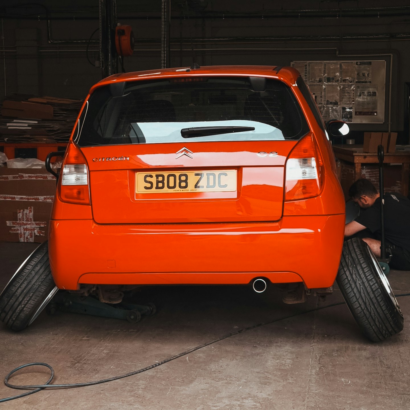 Mechanic repairs orange car elevated on a jack in repair shop.