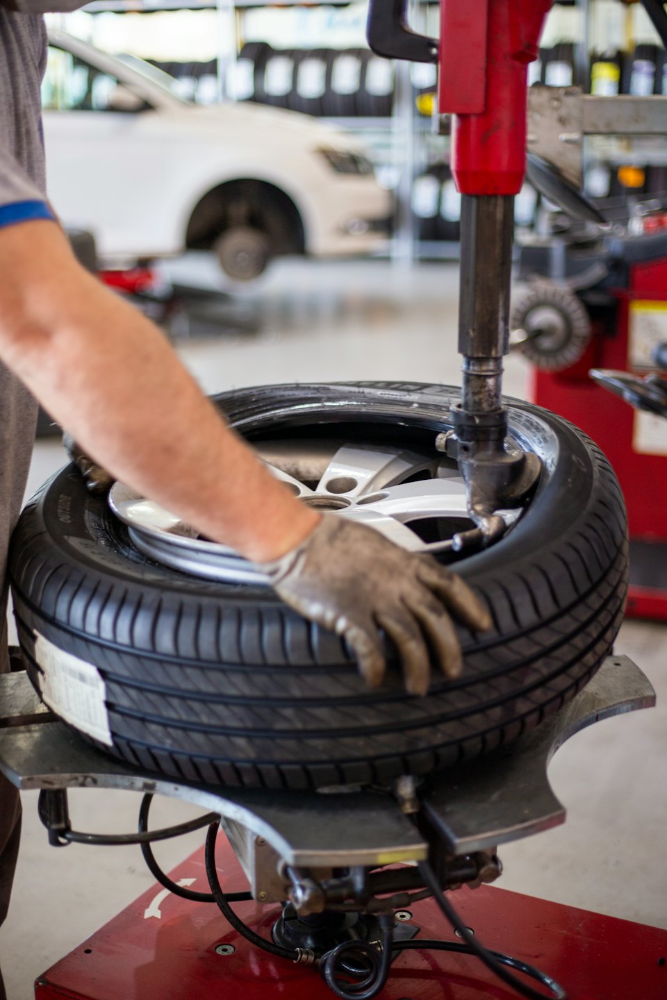 Mechanic mounts car tire onto alloy wheel with machine.
